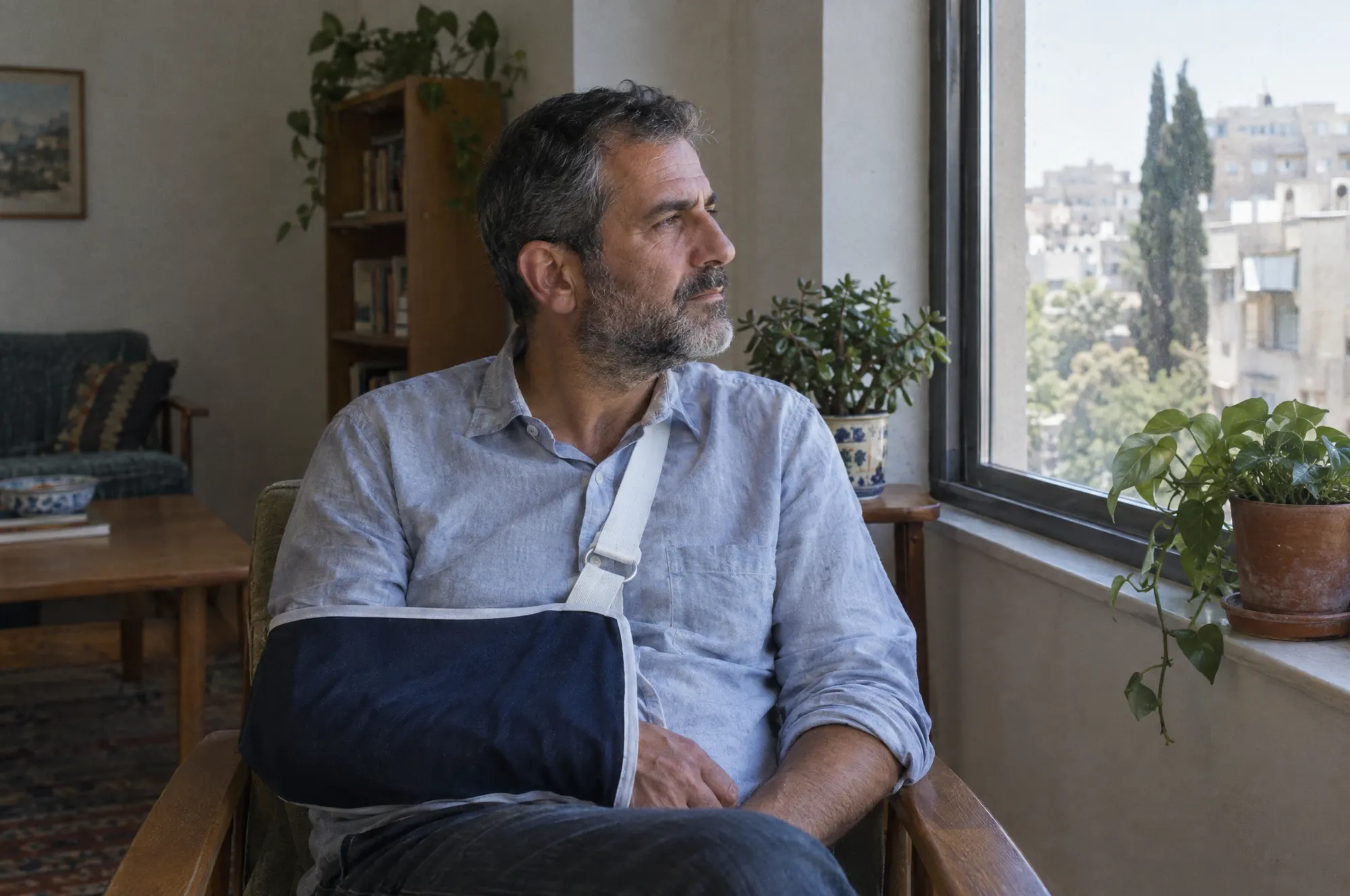 גבר עם יד בקלע יושב ליד החלון בביתו